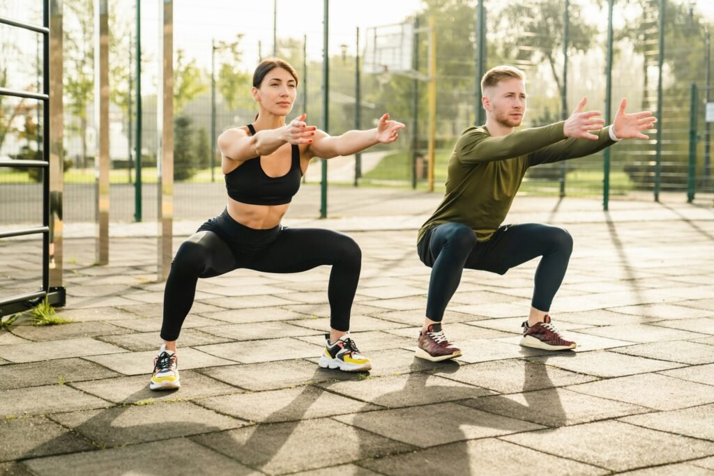 Two sporty caucasian 20s athletes doing warming-up excersises on sports ground in summer