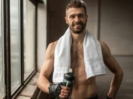 Happy man with towel and bottle of water after workout