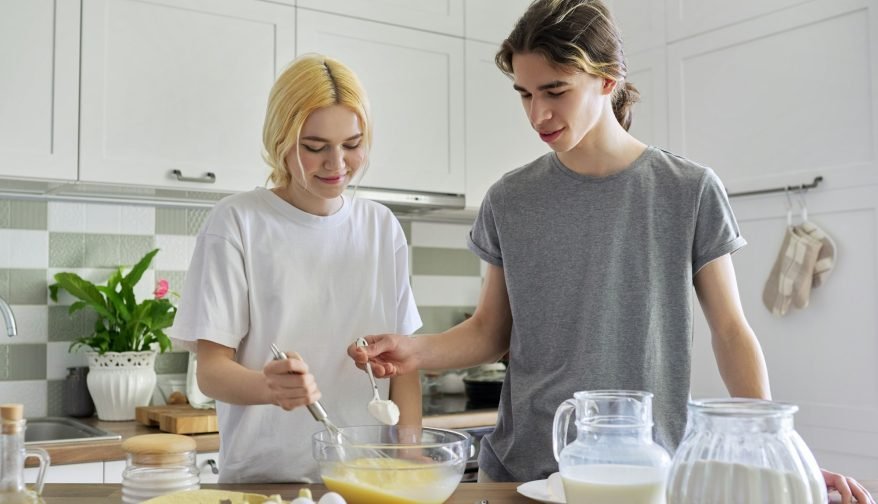 Teenagers guy and girl cooking pancakes in kitchen together